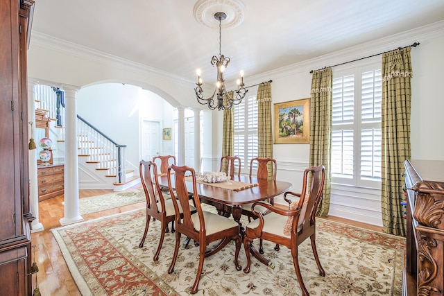 dining area featuring light wood finished floors, arched walkways, crown molding, and decorative columns