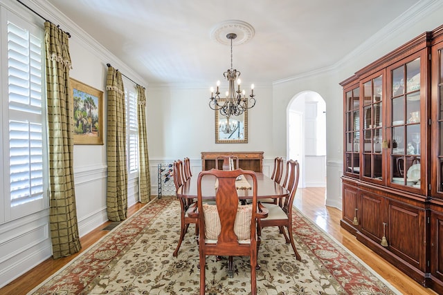 dining space with crown molding, a chandelier, a wainscoted wall, light wood-type flooring, and arched walkways