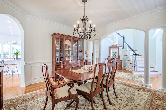 dining space with light wood-type flooring, decorative columns, wainscoting, and stairway