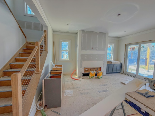 living area featuring stairway, a healthy amount of sunlight, and crown molding