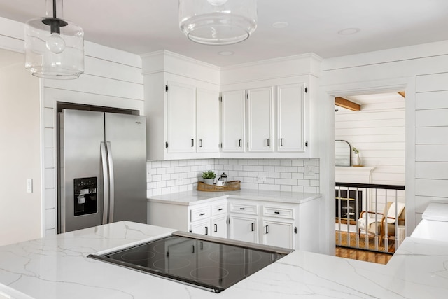 kitchen featuring stainless steel refrigerator with ice dispenser, hanging light fixtures, light stone countertops, black electric cooktop, and white cabinetry