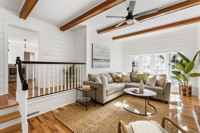 living room with ceiling fan, wooden walls, beamed ceiling, and wood-type flooring