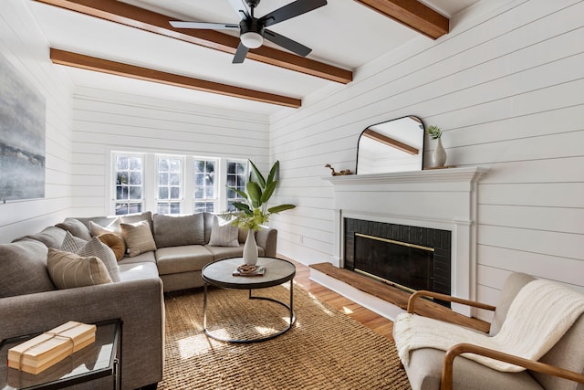 living room featuring hardwood / wood-style floors, wood walls, a brick fireplace, ceiling fan, and beam ceiling