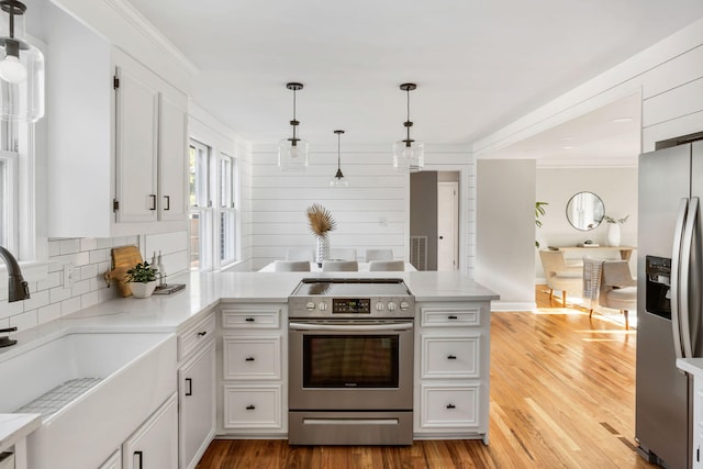 kitchen featuring white cabinetry, sink, hanging light fixtures, stainless steel appliances, and kitchen peninsula