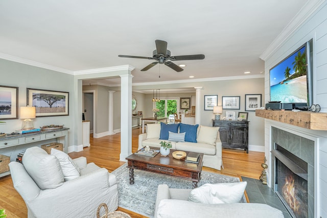 living room with a tile fireplace, wood finished floors, baseboards, ornate columns, and crown molding