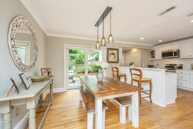 dining room featuring ornamental molding, baseboards, visible vents, and light wood finished floors