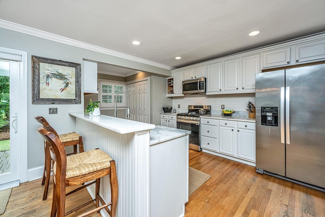 kitchen with light wood finished floors, appliances with stainless steel finishes, a peninsula, light countertops, and a kitchen bar