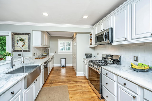 kitchen featuring stainless steel appliances, a sink, white cabinetry, ornamental molding, and light wood-type flooring