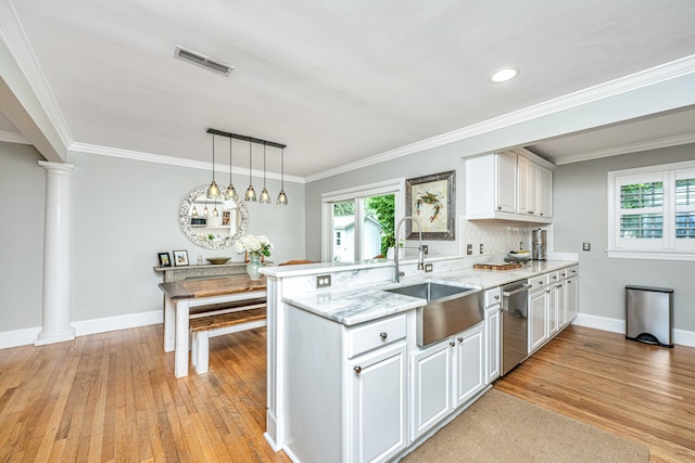 kitchen featuring visible vents, a peninsula, a sink, ornate columns, and a wealth of natural light