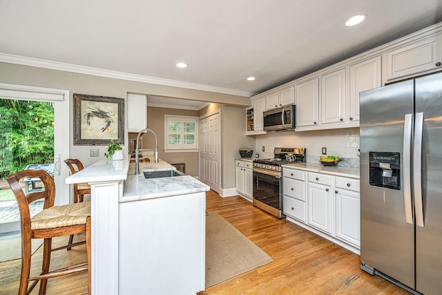 kitchen featuring light wood-style flooring, a sink, stainless steel appliances, white cabinetry, and backsplash