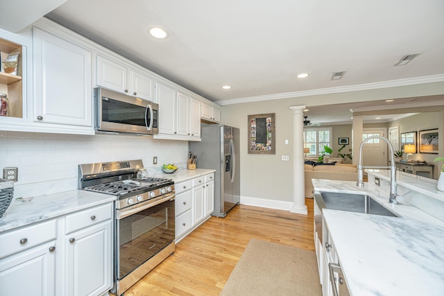 kitchen featuring stainless steel appliances, light wood-style floors, white cabinetry, and decorative columns