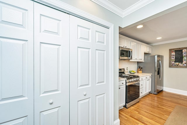 kitchen featuring light wood-style flooring, stainless steel appliances, white cabinetry, light countertops, and crown molding