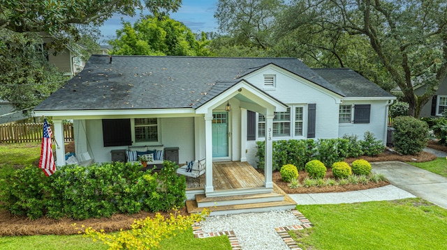 view of front of house featuring a shingled roof, covered porch, fence, a front lawn, and brick siding