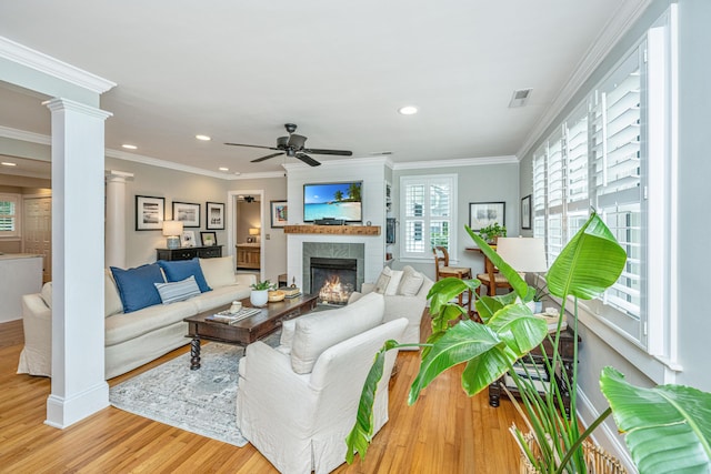 living room featuring visible vents, ornamental molding, wood finished floors, a lit fireplace, and ornate columns