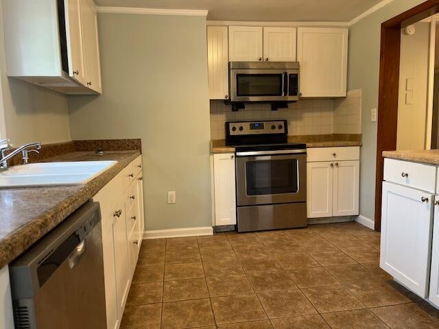 kitchen featuring dark tile patterned floors, crown molding, sink, stainless steel appliances, and white cabinets