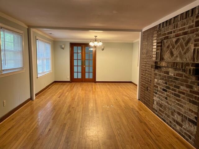 spare room featuring french doors, an inviting chandelier, light wood-type flooring, and crown molding