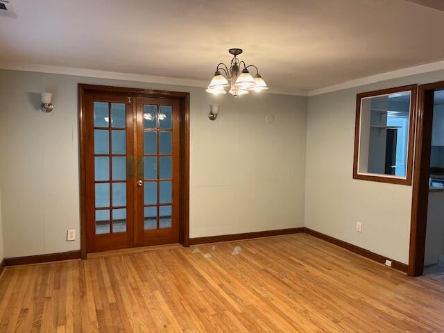 empty room with french doors, ornamental molding, a chandelier, and light hardwood / wood-style floors