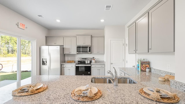 kitchen featuring appliances with stainless steel finishes, gray cabinets, light stone countertops, and sink