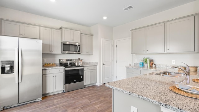 kitchen with sink, hardwood / wood-style flooring, gray cabinetry, stainless steel appliances, and light stone counters