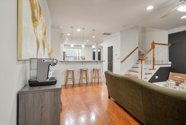 living area featuring stairway, light wood-style floors, visible vents, and ornamental molding