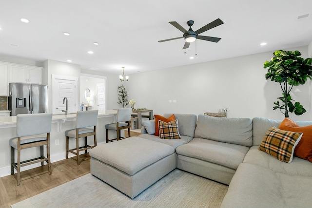 living room featuring ceiling fan with notable chandelier, light hardwood / wood-style floors, and sink