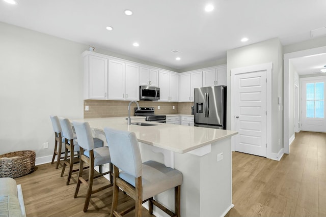 kitchen with a breakfast bar, kitchen peninsula, light wood-type flooring, appliances with stainless steel finishes, and white cabinets