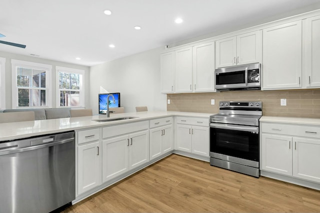 kitchen featuring kitchen peninsula, sink, white cabinetry, light wood-type flooring, and stainless steel appliances