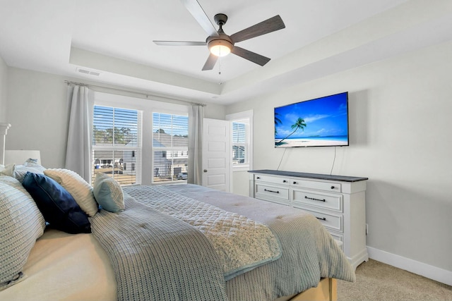 bedroom with ceiling fan, light colored carpet, and a raised ceiling