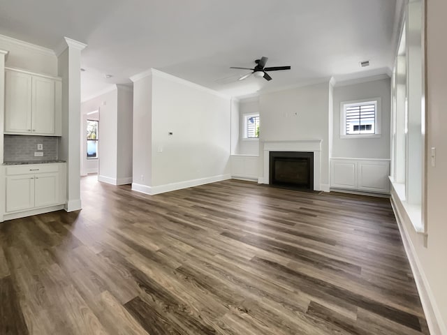 unfurnished living room with dark wood-style floors, ornamental molding, and a wealth of natural light