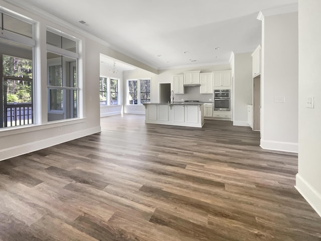 unfurnished living room with a sink, baseboards, ornamental molding, and dark wood finished floors