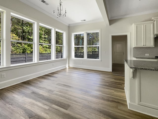 unfurnished dining area featuring baseboards, visible vents, ornamental molding, and wood finished floors