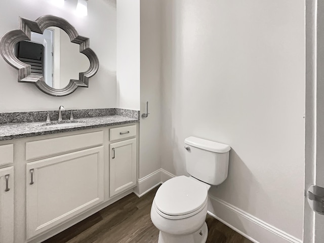half bath with baseboards, vanity, toilet, and wood finished floors