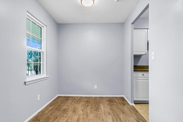 spare room with light wood-type flooring, a textured ceiling, and baseboards