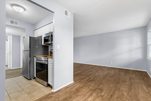 kitchen with stainless steel appliances, visible vents, baseboards, light wood-style floors, and white cabinetry