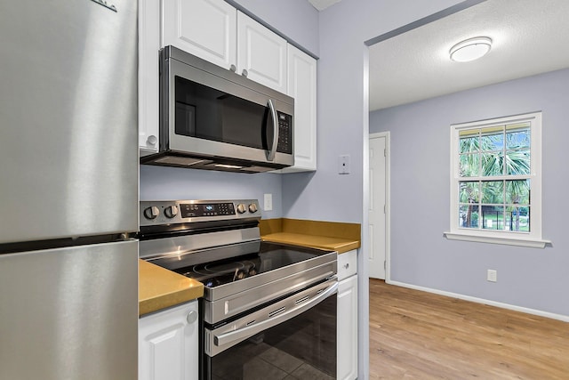 kitchen with stainless steel appliances, baseboards, white cabinets, and light wood finished floors