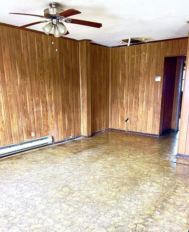 empty room with a textured ceiling, baseboard heating, ceiling fan, and wood walls