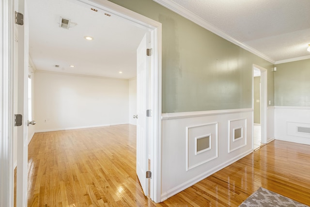 hallway featuring crown molding, light hardwood / wood-style flooring, and a textured ceiling