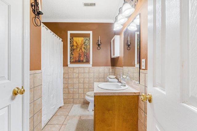 bathroom featuring tile patterned floors, crown molding, toilet, vanity, and tile walls