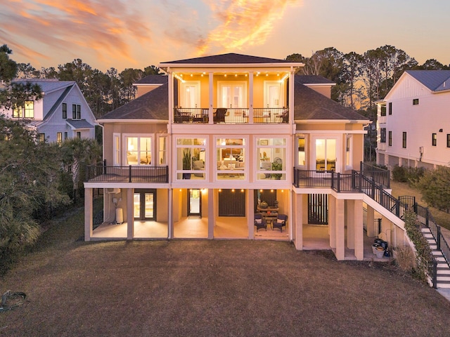 back house at dusk featuring a yard, a patio area, and a balcony