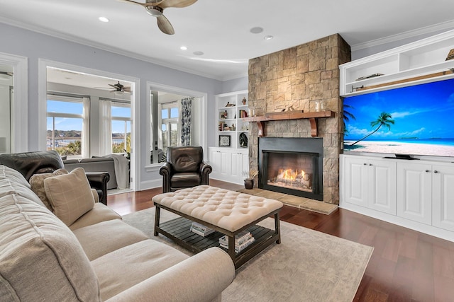 living room featuring ceiling fan, dark wood-type flooring, crown molding, built in features, and a fireplace