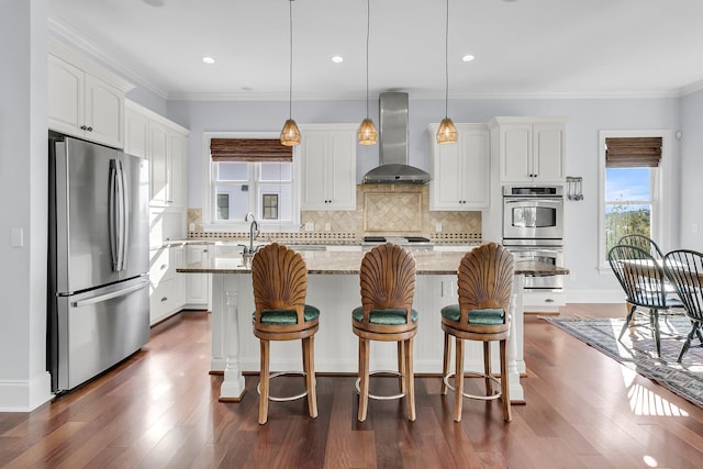 kitchen featuring wall chimney range hood, a kitchen island, light stone counters, white cabinetry, and stainless steel appliances