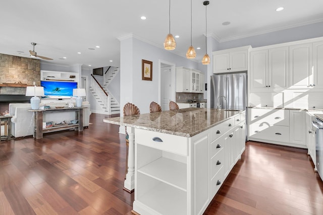 kitchen featuring white cabinetry, light stone countertops, ceiling fan, decorative light fixtures, and a center island with sink