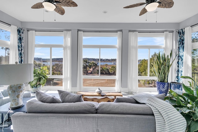 sunroom with ceiling fan and a water view