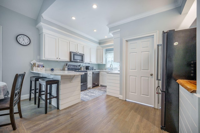 2177 Gulf Dr, Mount Pleasant, SC 29464 - kitchen featuring appliances with stainless steel finishes, a peninsula, crown molding, a kitchen breakfast bar, and light wood-style floors