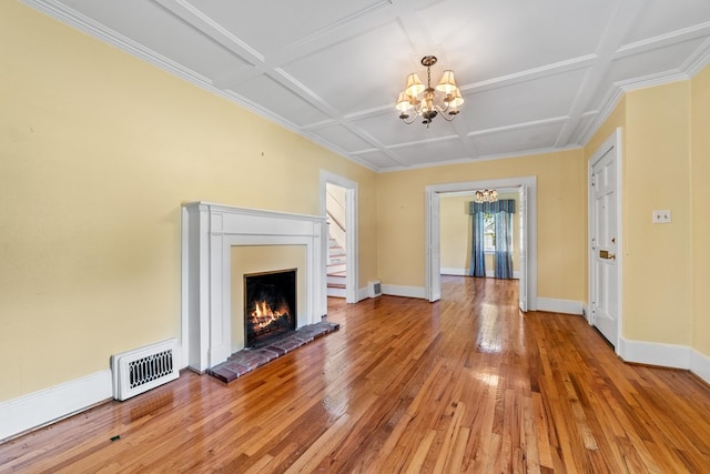 unfurnished living room with a brick fireplace, a chandelier, coffered ceiling, hardwood / wood-style flooring, and crown molding