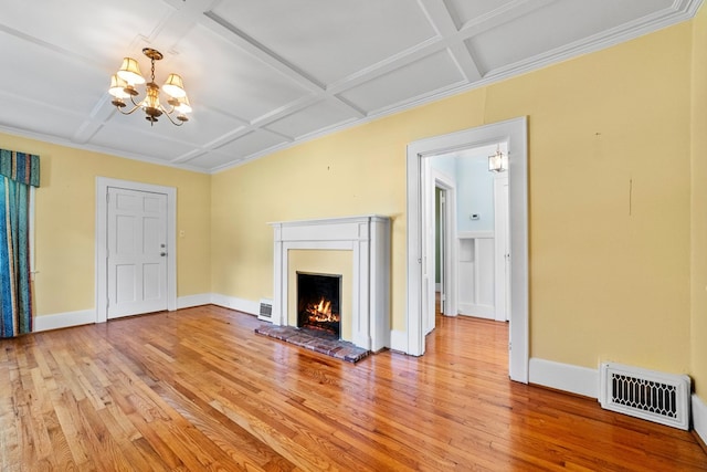 unfurnished living room featuring a brick fireplace, light hardwood / wood-style floors, a notable chandelier, coffered ceiling, and ornamental molding