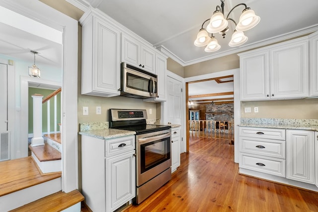 kitchen with pendant lighting, light hardwood / wood-style flooring, a fireplace, appliances with stainless steel finishes, and white cabinetry