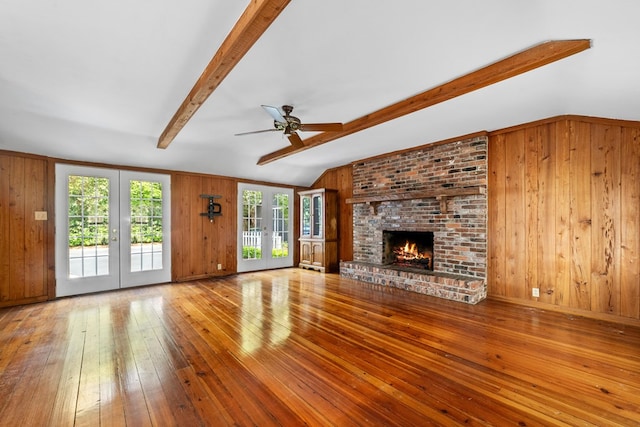 unfurnished living room with french doors, wood walls, light hardwood / wood-style floors, and lofted ceiling with beams