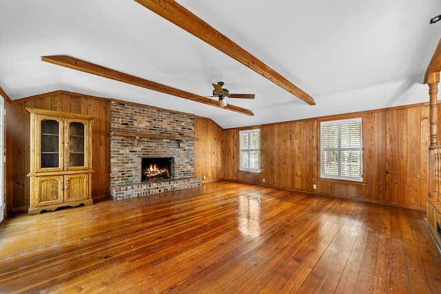 unfurnished living room featuring wood walls, a brick fireplace, ceiling fan, wood-type flooring, and vaulted ceiling with beams