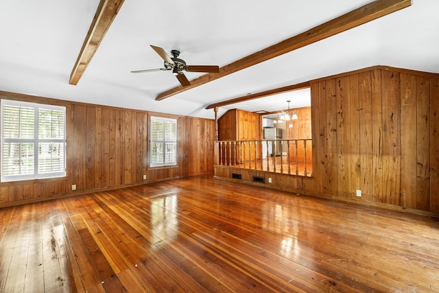 unfurnished living room with ceiling fan with notable chandelier, hardwood / wood-style floors, vaulted ceiling with beams, and wooden walls